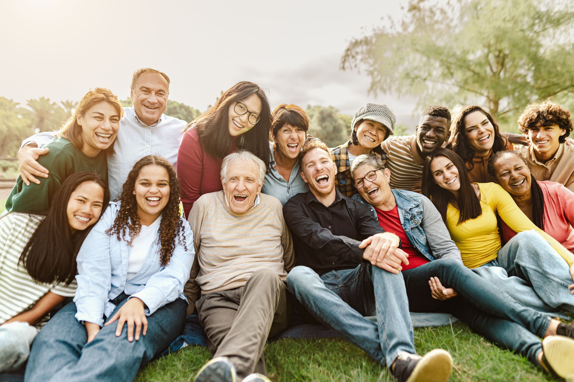 Personas multigeneracionales felices divirtiéndose sentadas en el césped de un parque público